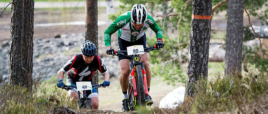 Två MTB-cyklister cyklar uppför i skogen