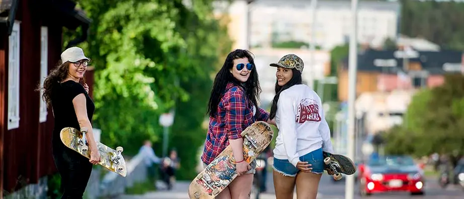Tre tjejer med skateboard går på Gruvgatan i centrala Falun