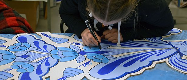 En elev sitter och målar blått kurbitsmotiv på en trätavla.